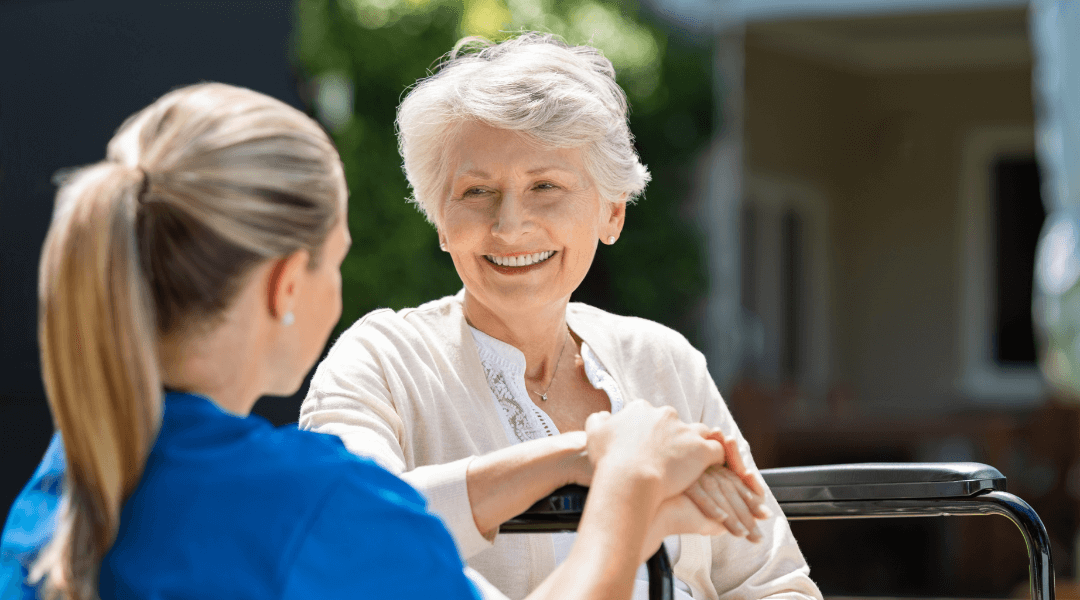 Lächelnde Seniorin hält die Hand ihrer Pflegekraft im Freien.